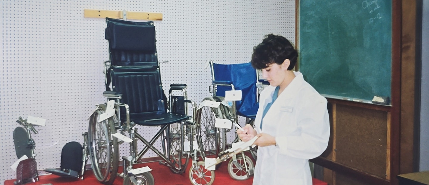 1995 image of a woman with short dark hair in front of two wheelchairs.