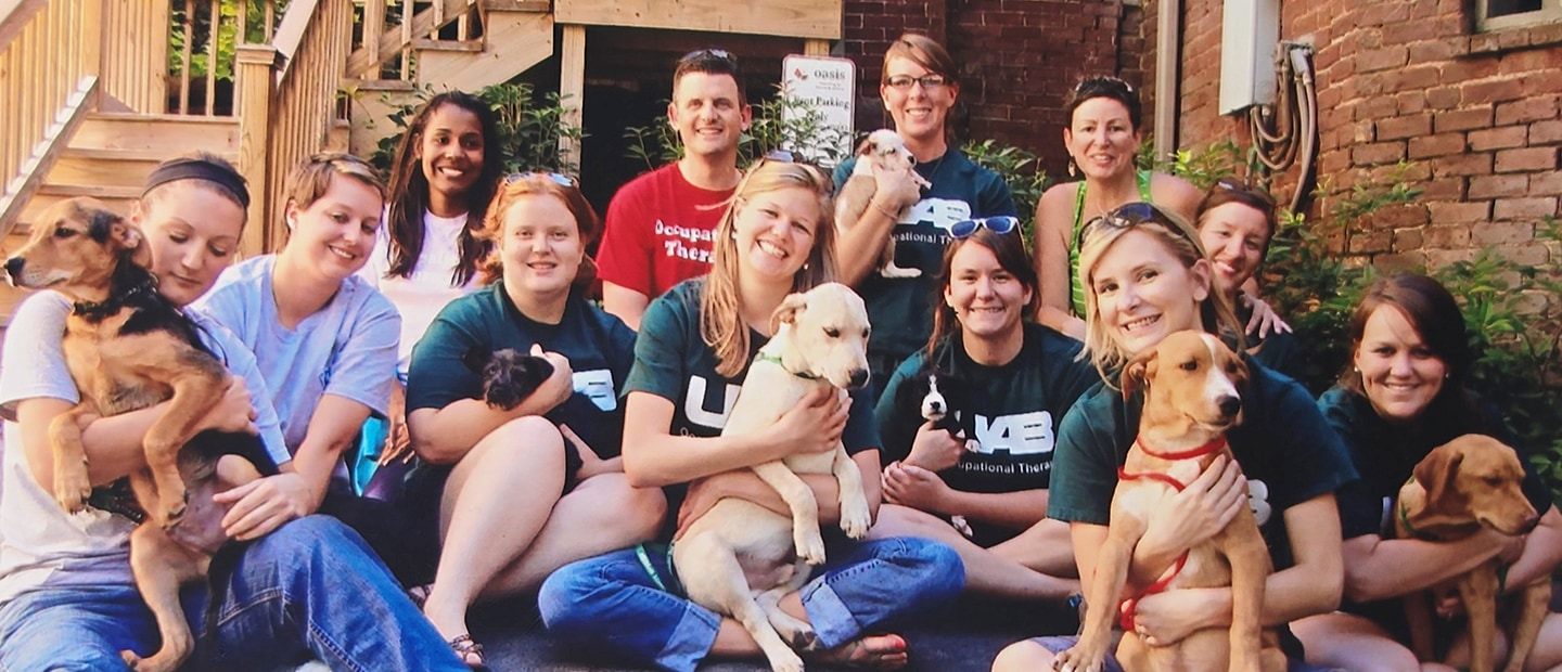 A group of students in 2011 sitting outside, several of them hugging dogs.