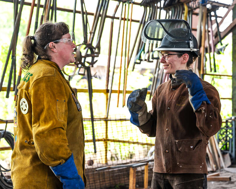 Two women in heavy safety gear at a metal casting location.