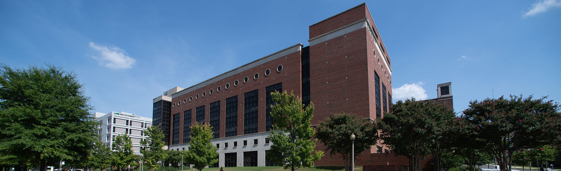 The Ryals Building housing the UAB School of Public Health against a bright blue sky, surrounded by trees.