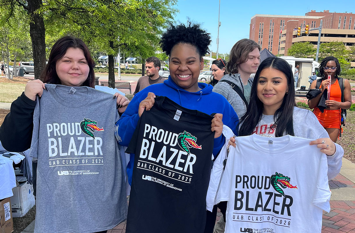 Three female students holding up tshirts reading "proud blazer."