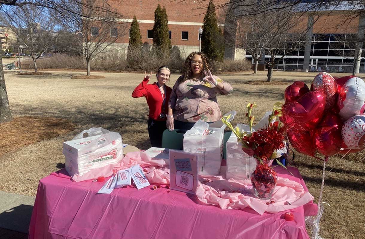 Two female students outside at valentine's day-themed table.