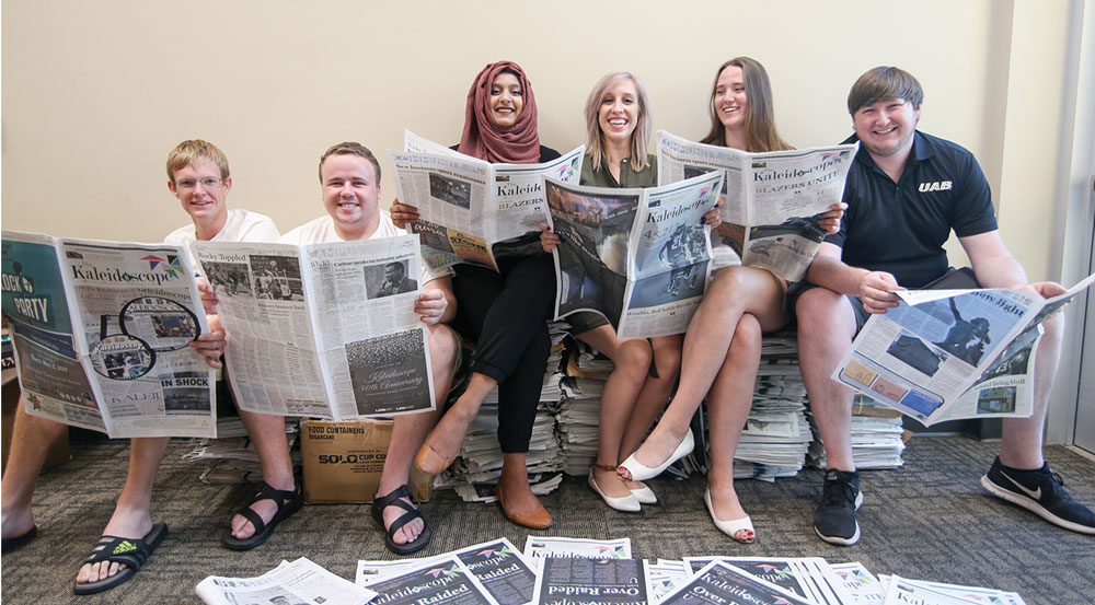 Photo of 2017-2018 Kaleidoscope staff looking at newspapers and sitting on newspaper stacks