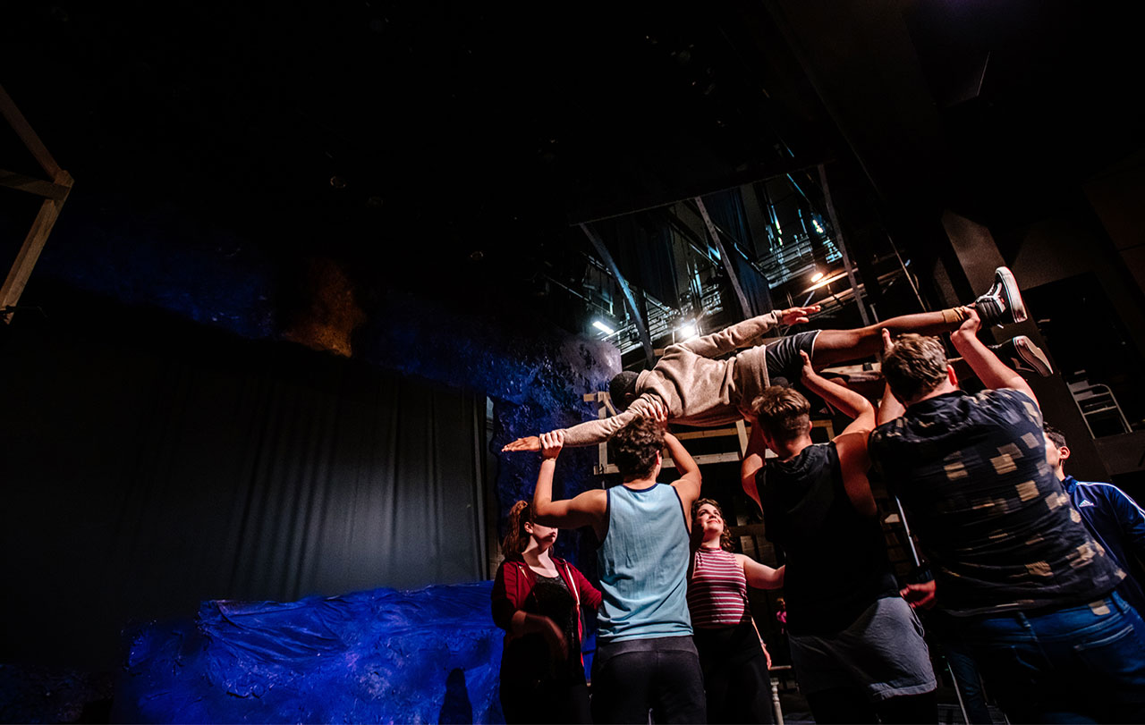 Photo of student actors lifting actor over their heads during rehearsal