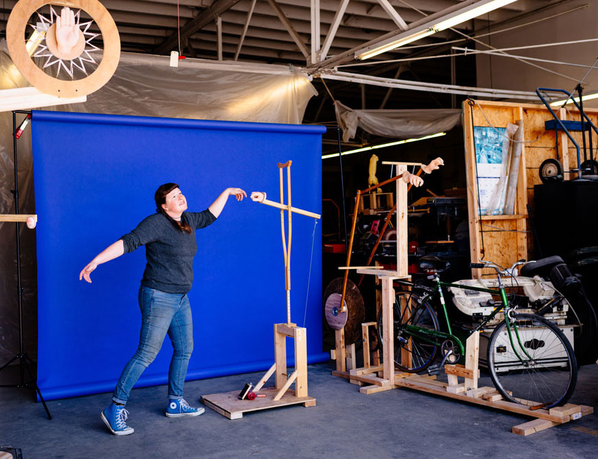 Photo of Stacey Holloway in garage recreating Adam and God image from Sistine Chapel with one of her sculptures