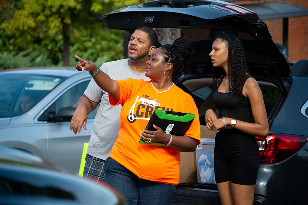 Photo of volunteer helping new arrivals as they begin to unload their car trunk