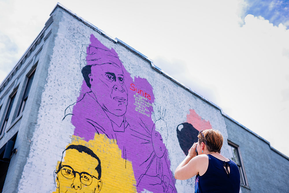 Photo of Viktoria Havasi taking picture of Avondale mural showing colorful portraits of people