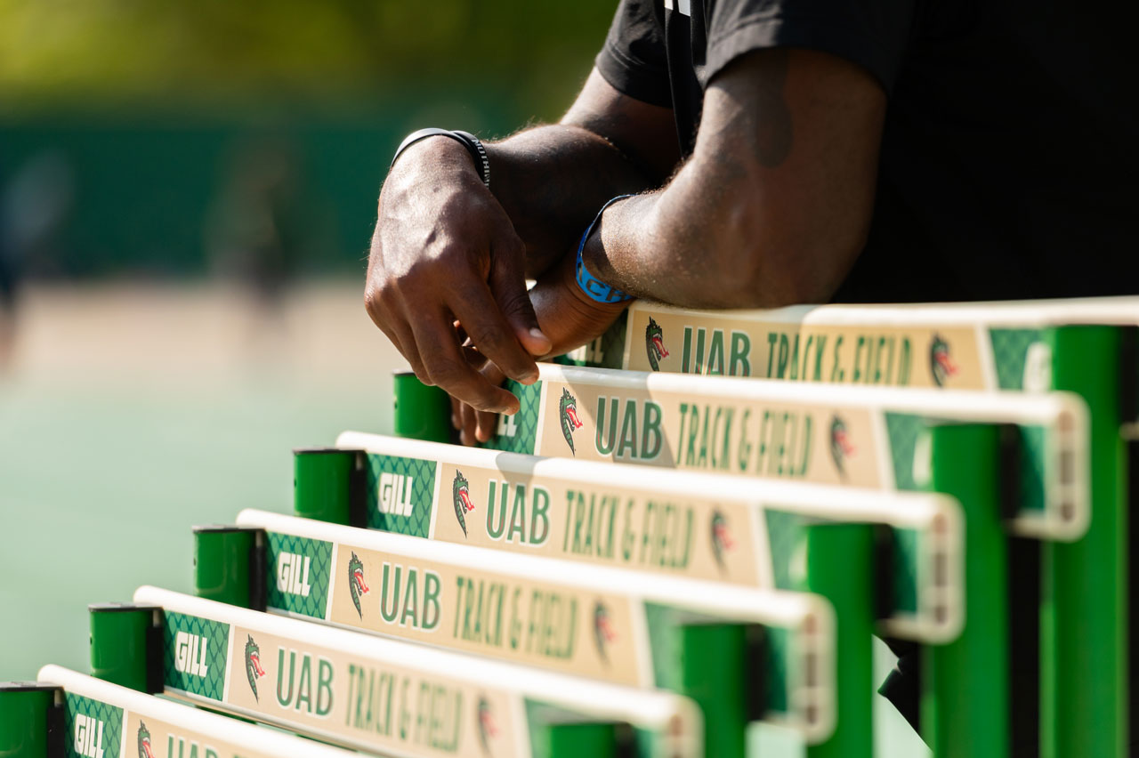 Close-up of arms leaning on stacked Track and Field hurdles with UAB Blazers Track and Field branding on them at PNC Field.